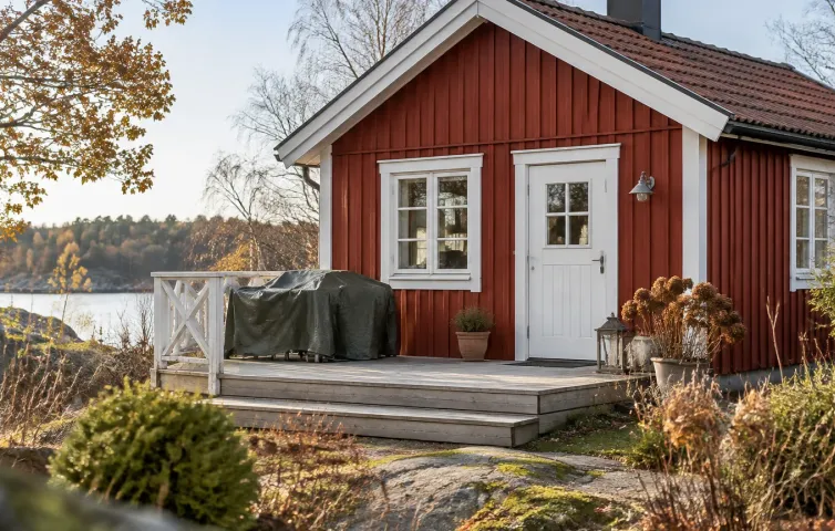 Litet nordiskt sommarhus med stängd dörr och övertäckta utemöbler på trallen